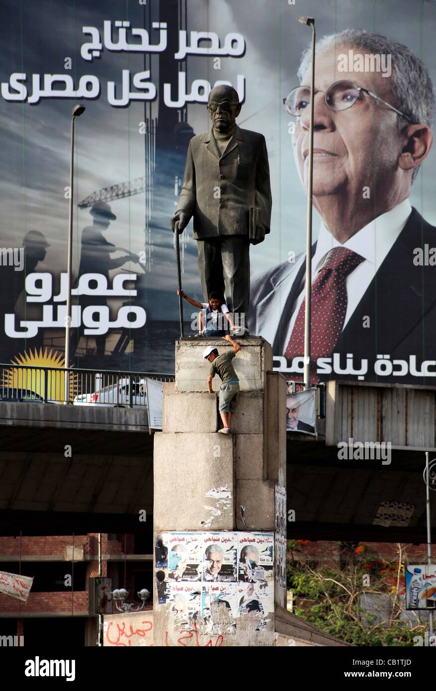 Mayo 21, 2012 - El Cairo, Cairo, Egipto - Egipto chicos sentarse debajo de una estatua del novelista egipcio Naguib Mahfouz visto delante de un enorme estandarte de la campaña electoral para el ex ministro de relaciones exteriores y jefe de la Liga Árabe y candidato presidencial, Amr Mussa, en El Cairo el 21 de mayo de 2012. El Consejo Supremo de th Foto de stock