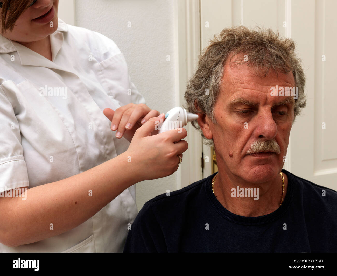 Una enfermera colocando un termómetro en el tímpano del oído del paciente tomando su temperatura Foto de stock