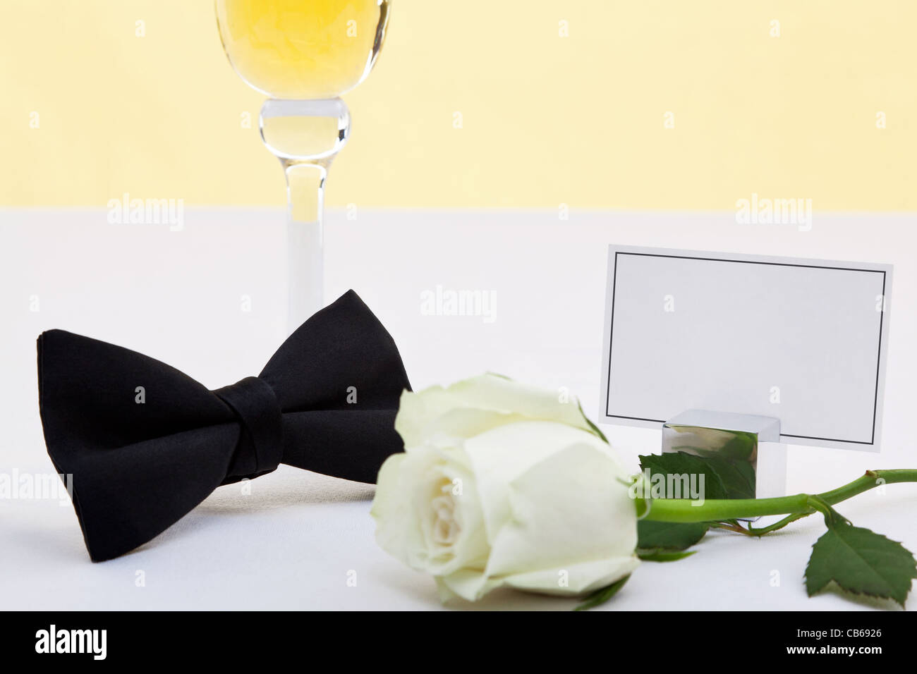 Foto de una pajarita negra, rosa blanca, una copa de champán y una tarjeta en blanco para añadir su propio mensaje. Foto de stock