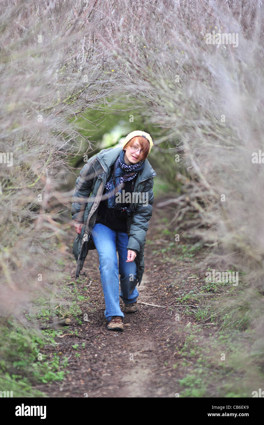 Mujer joven caminando dentro del túnel de ramas de Bush, llevar cámara Leica Foto de stock