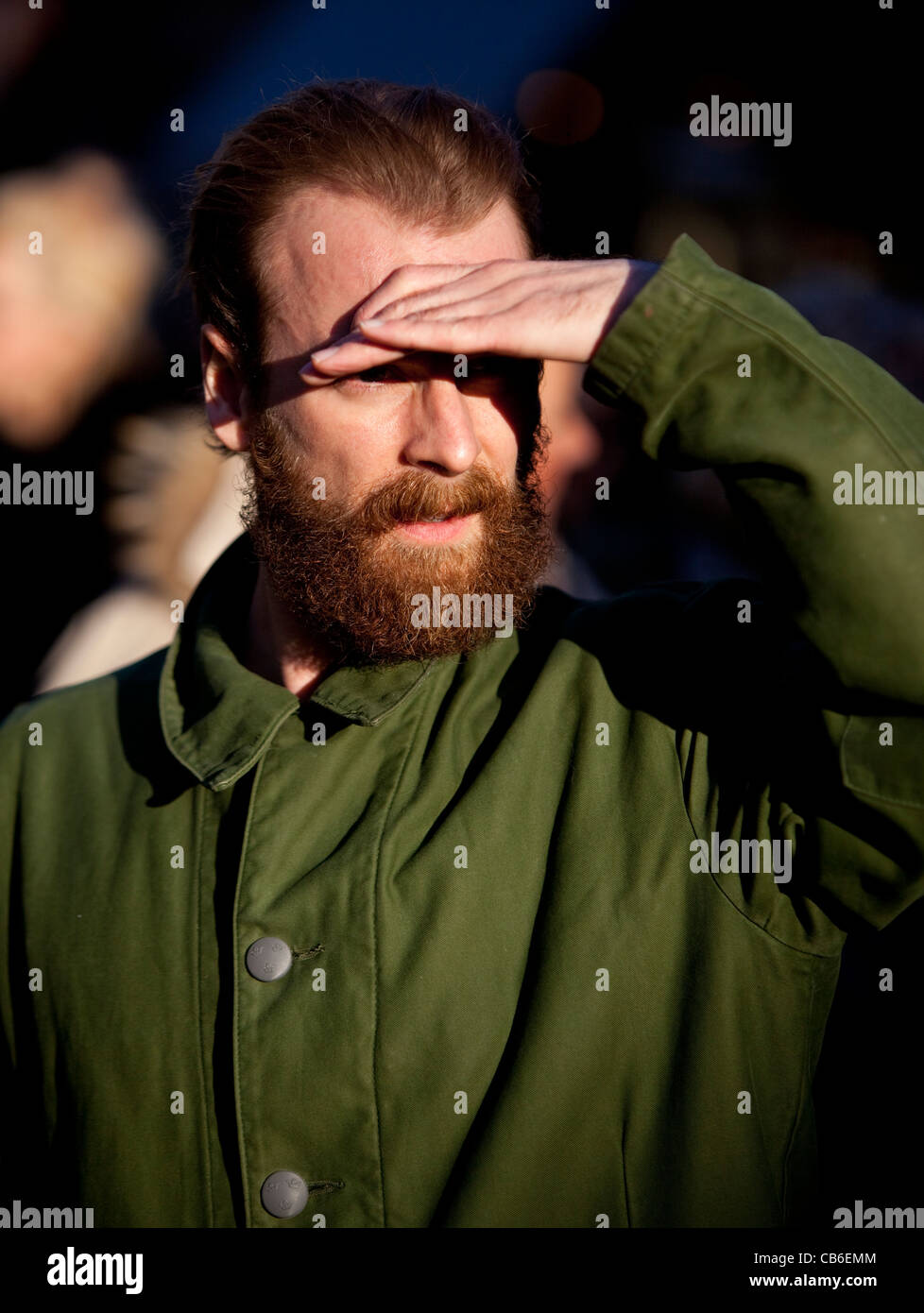 Hombre barbudo cegado por el sol cubriendo sus ojos con la mano como visera. Foto de stock