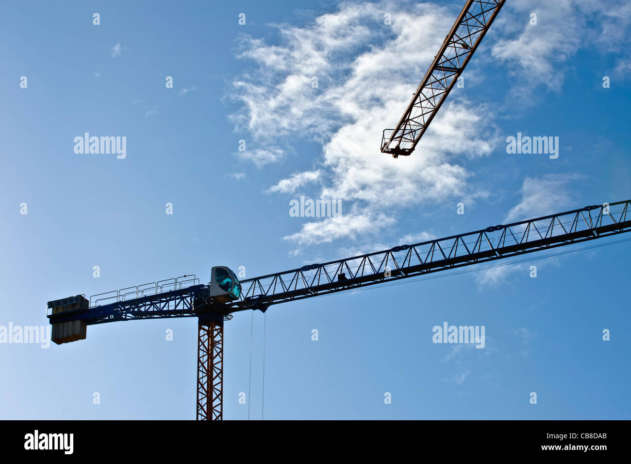 Siluetas de grúas de construcción contra un cielo azul Foto de stock