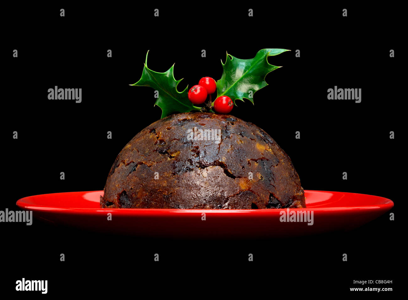 Foto de un pudín de Navidad con acebo encima aislado sobre un fondo negro. Foto de stock