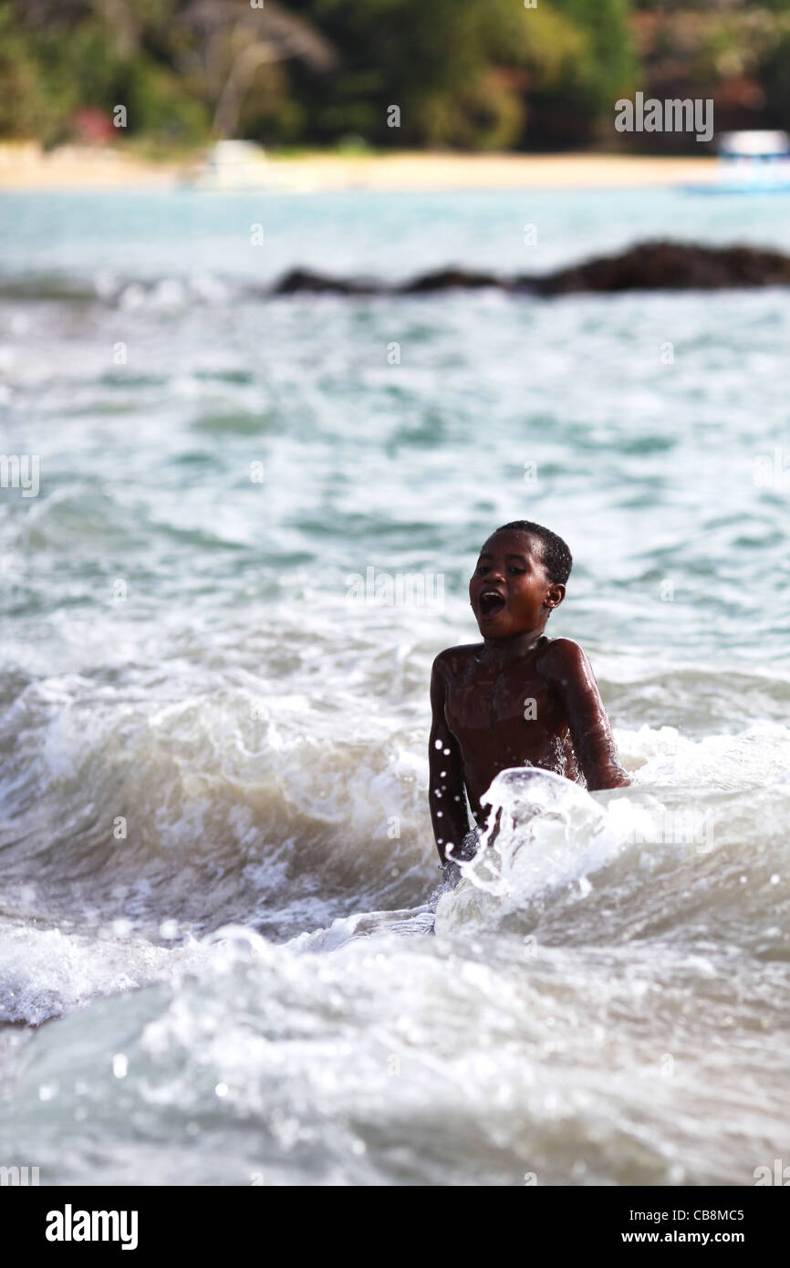 Un sorprendido medio sumergida joven obteniendo engullido por el agua fría en la playa de surf en Nosy Komba, Madagascar, África Foto de stock