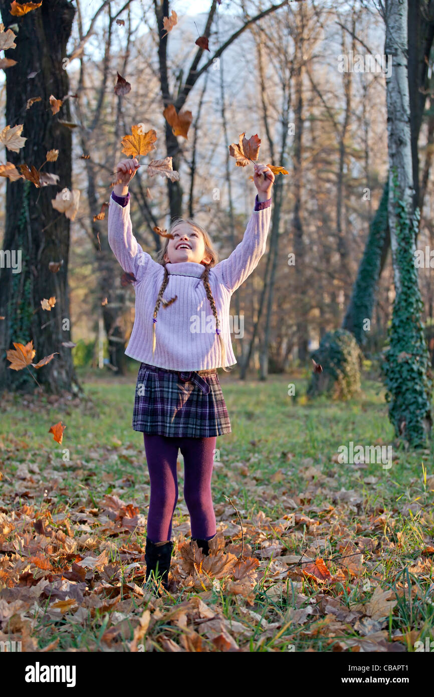 Chica está jugando en el bosque con el follaje de otoño Foto de stock