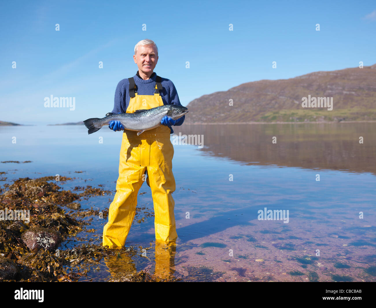 Pescador sosteniendo el salmón por el lago Foto de stock