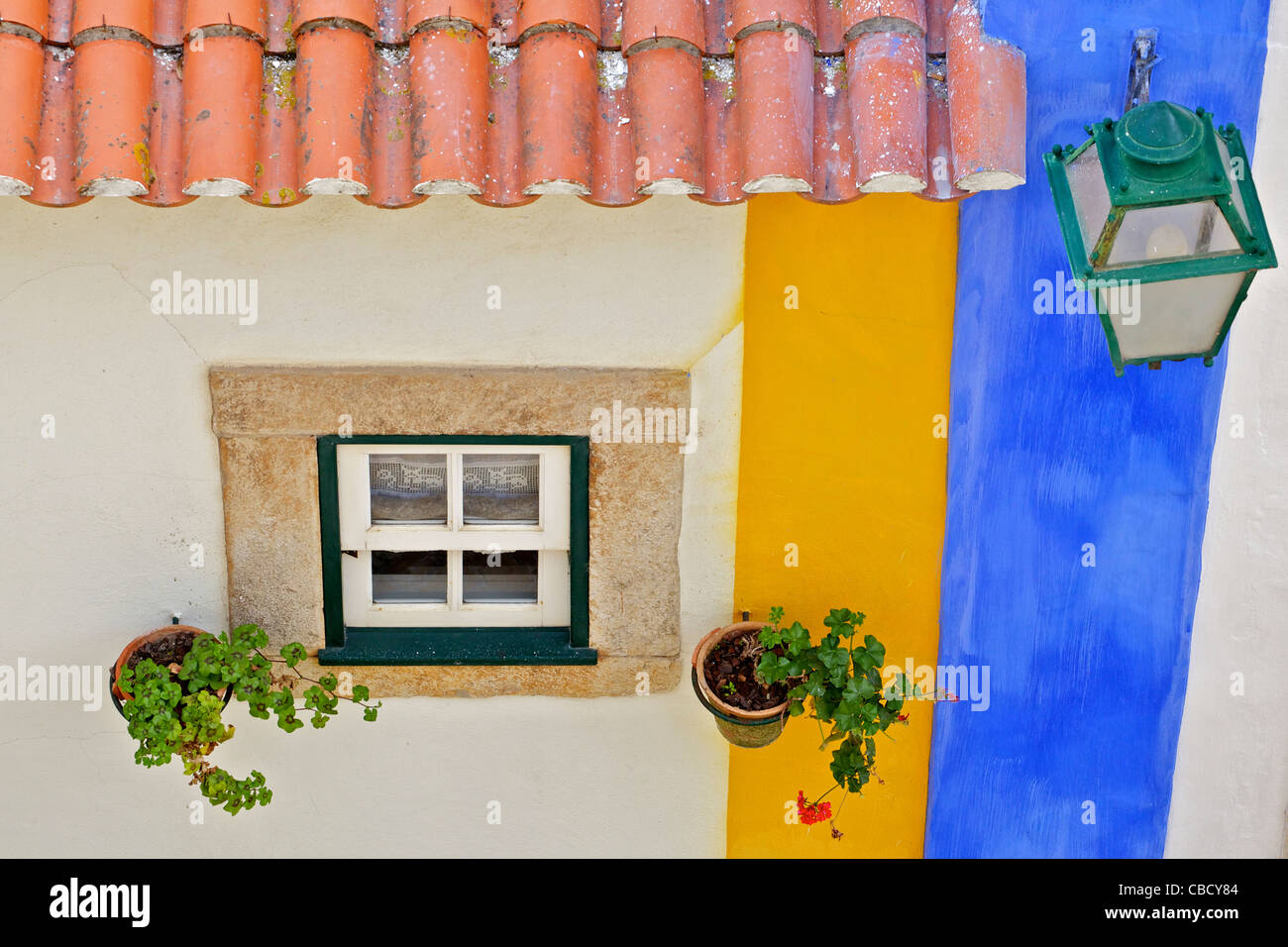 Ventana, lámpara de la calle y un techo de tejas de arcilla con una pared de color pastel en el pueblo medieval de Obidos. Foto de stock