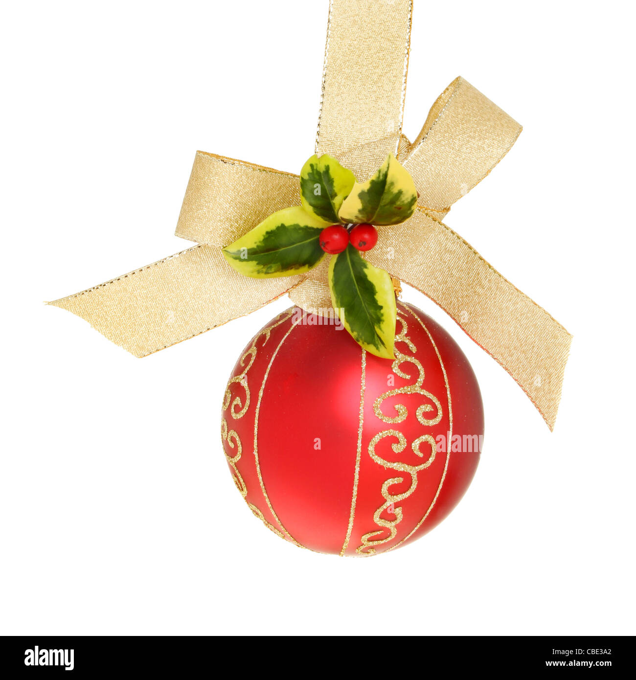 Adornos de Navidad en rojo y dorado con una cinta de oro entrelazados en un arco con una ramita de acebo fresco contra un blanco aislado Foto de stock