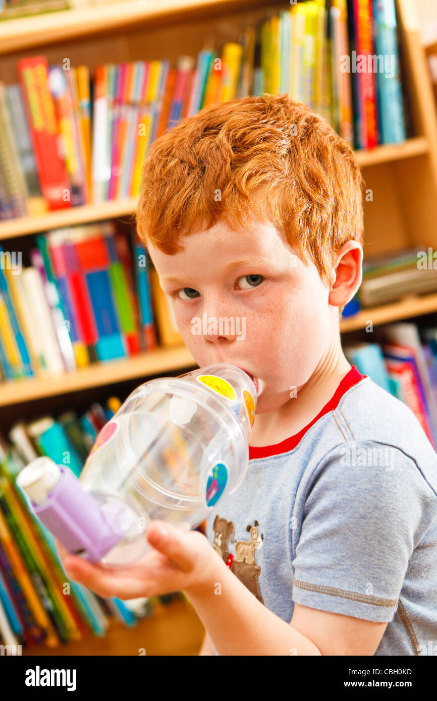 Joven, de 7 años, usando un inhalador para combatir el asma. Auto medicar. Foto de stock