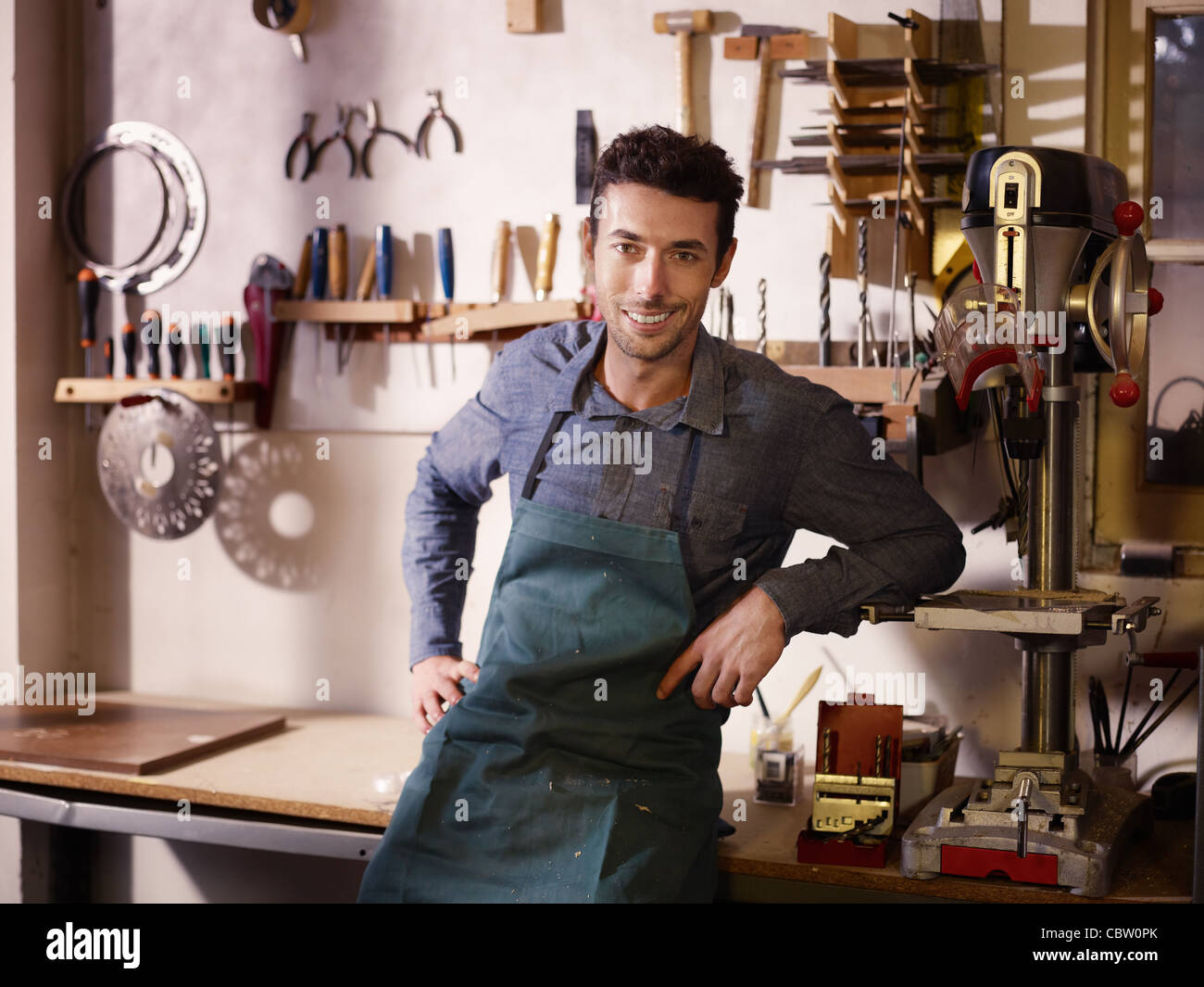 Retrato del hombre adulto en el trabajo como artesano en la tienda con herramientas en segundo plano. Foto de stock