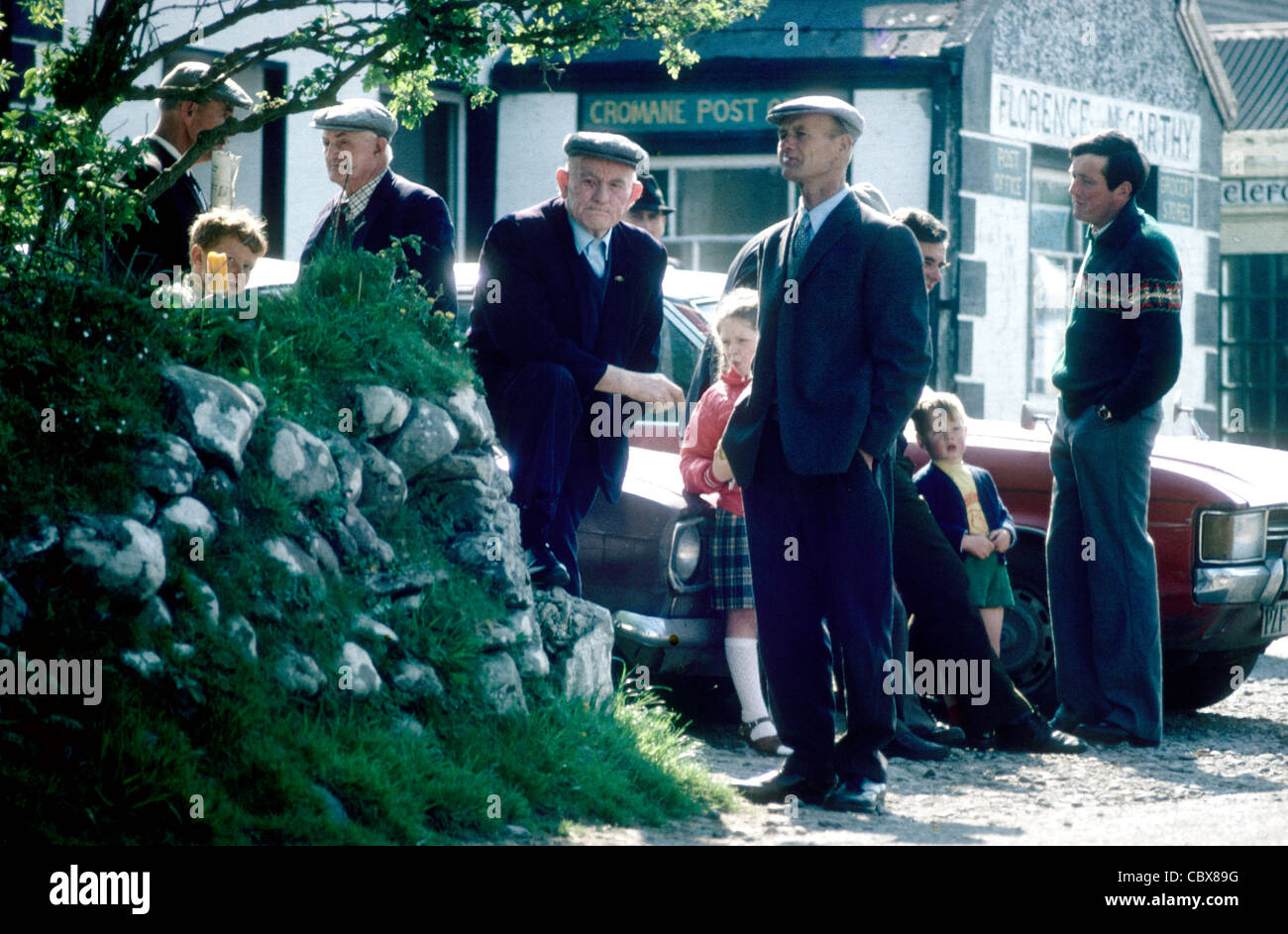 Un grupo de hombres y muchachos se reúnen en torno a la oficina de correos después de la misa dominical en Cromane Co Kerry Irlanda Foto de stock