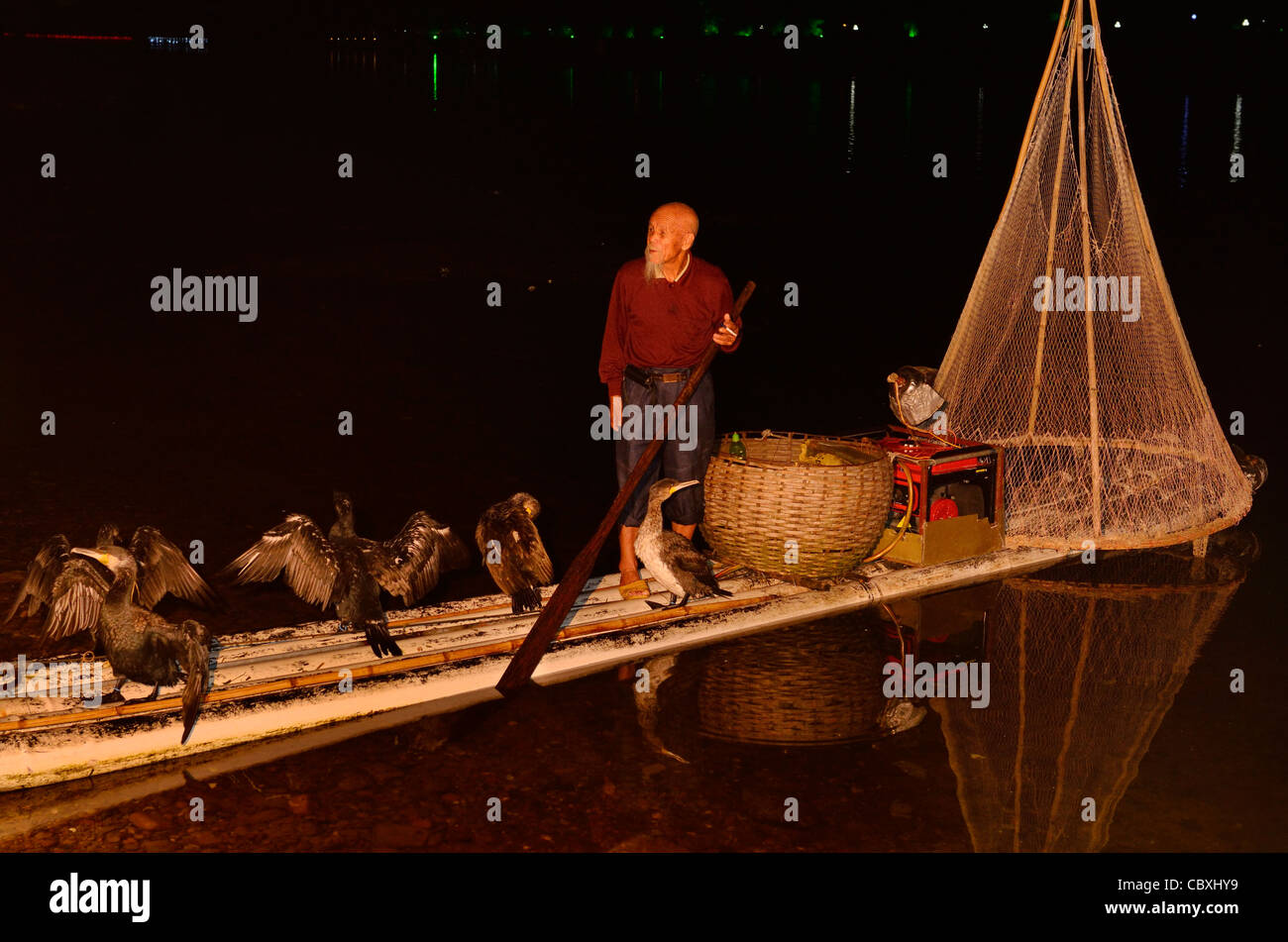 Pescador chino con cormorán aves y net en una balsa de bambú en Yangshuo China por la noche en el río Li. Foto de stock
