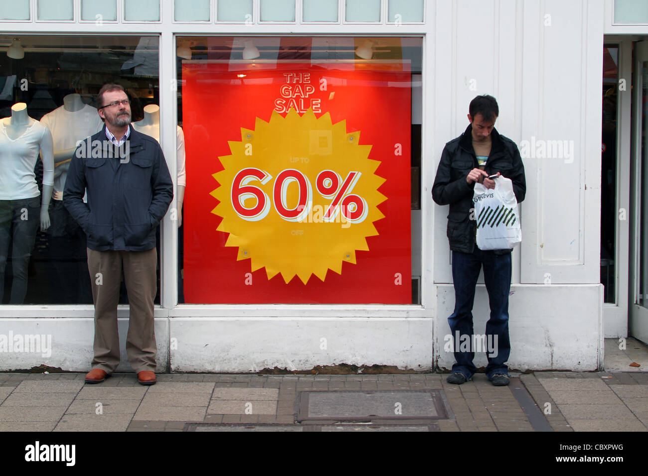Aburrido parejas masculinas están de pie y esperan fuera de las tiendas durante el mes de enero las ventas en Cambridge Foto de stock
