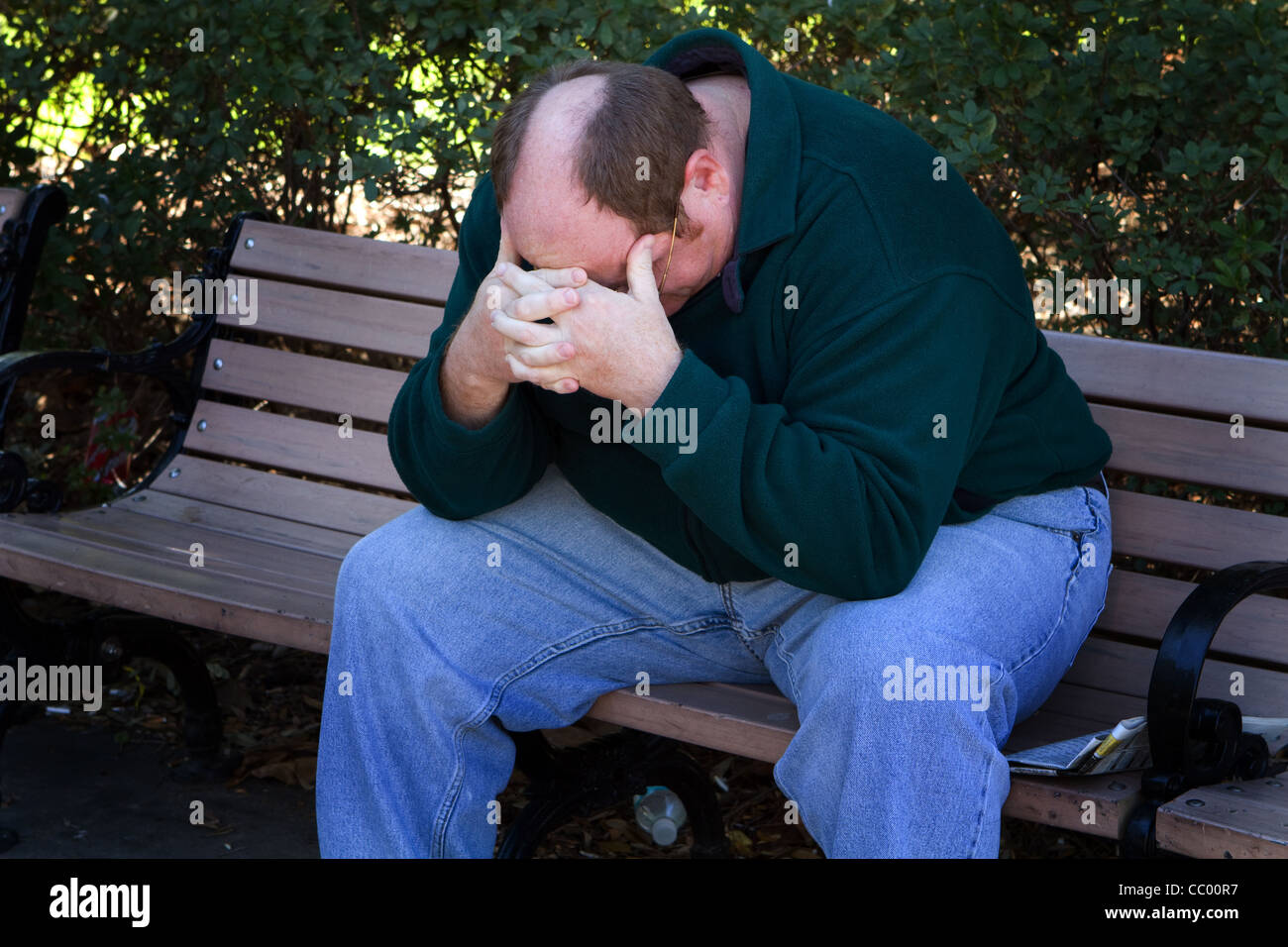 Hombre sin hogar se asienta en una zona trash de un parque en un estado de ánimo deprimido. Foto de stock