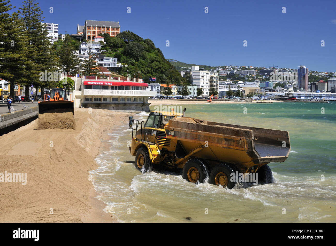 Camión que conduce a través de agua de mar y olas en el trabajo de reabastecimiento de la playa (la playa tiene un nuevo lote de arena) en Oriental Bay, Wellington, Nueva Zelanda. Foto de stock