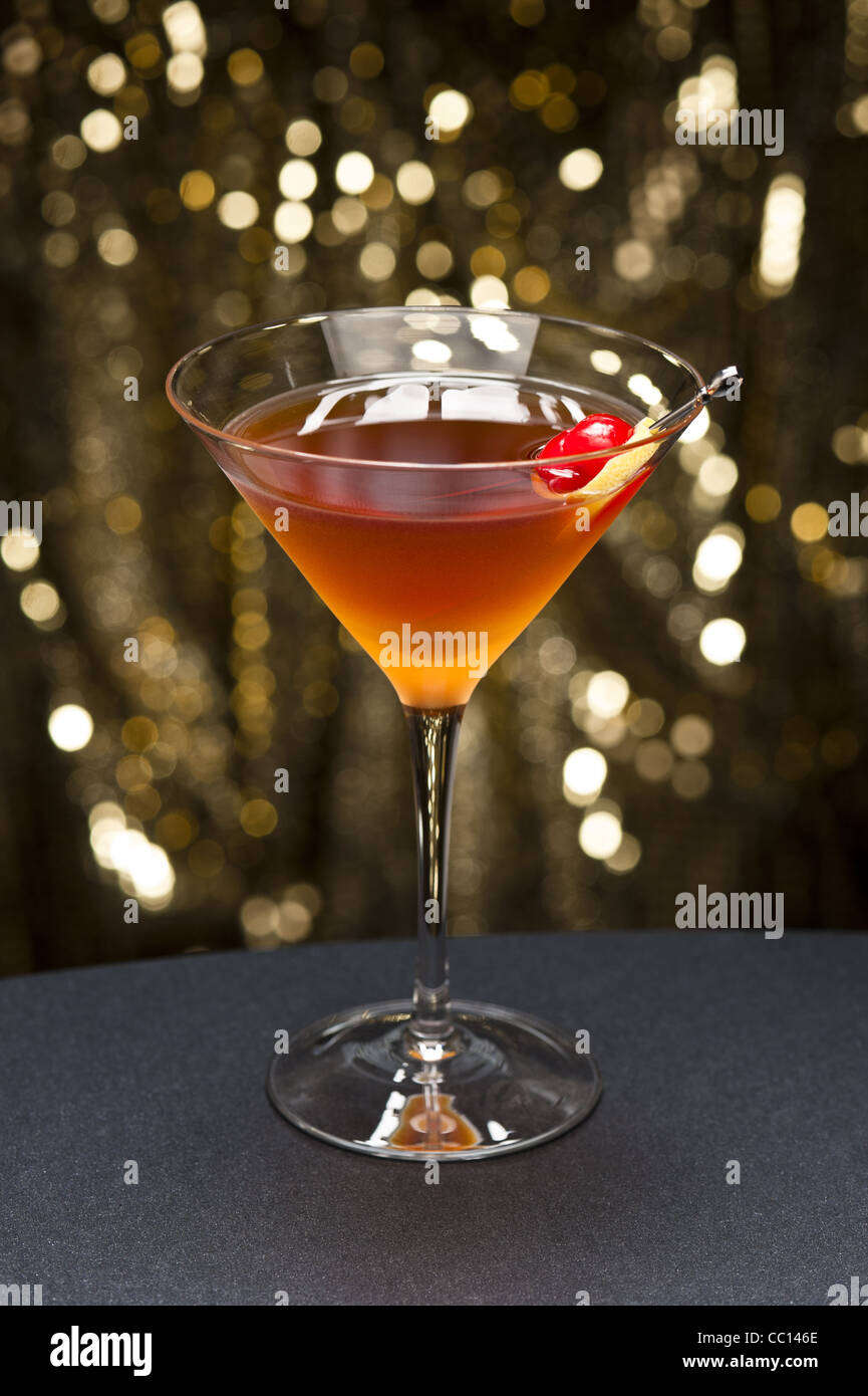 Manhattan cóctel aderezado con una cereza y limón y oro glitter back ground Foto de stock