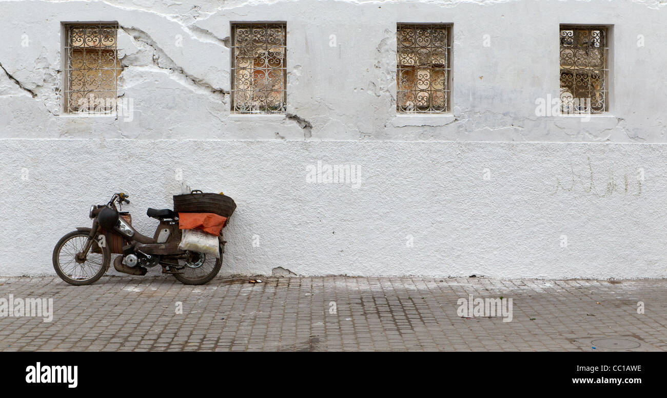 Antigua y en lugar de un solo cilindro oxidado motocicletas o ciclomotores apoyado contra una pared blanca en El Jadida, Marruecos Foto de stock