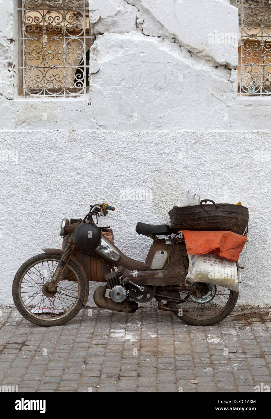 Antigua y en lugar de un solo cilindro oxidado motocicletas o ciclomotores apoyado contra una pared blanca en El Jadida, Marruecos Foto de stock