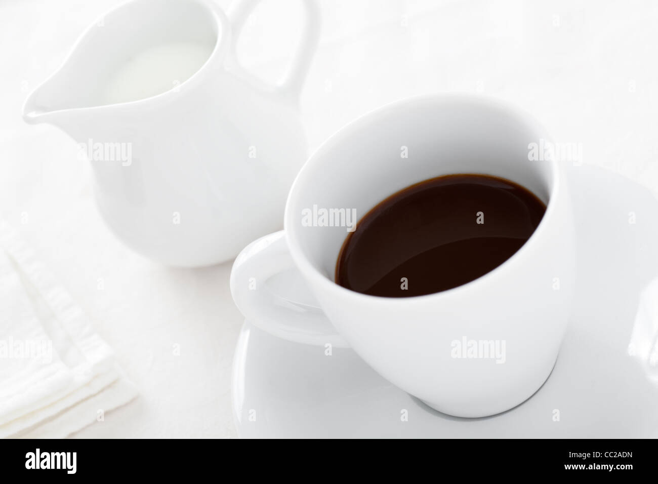 Taza de café con leche de la jarra sobre fondo blanco, High Key Foto de stock
