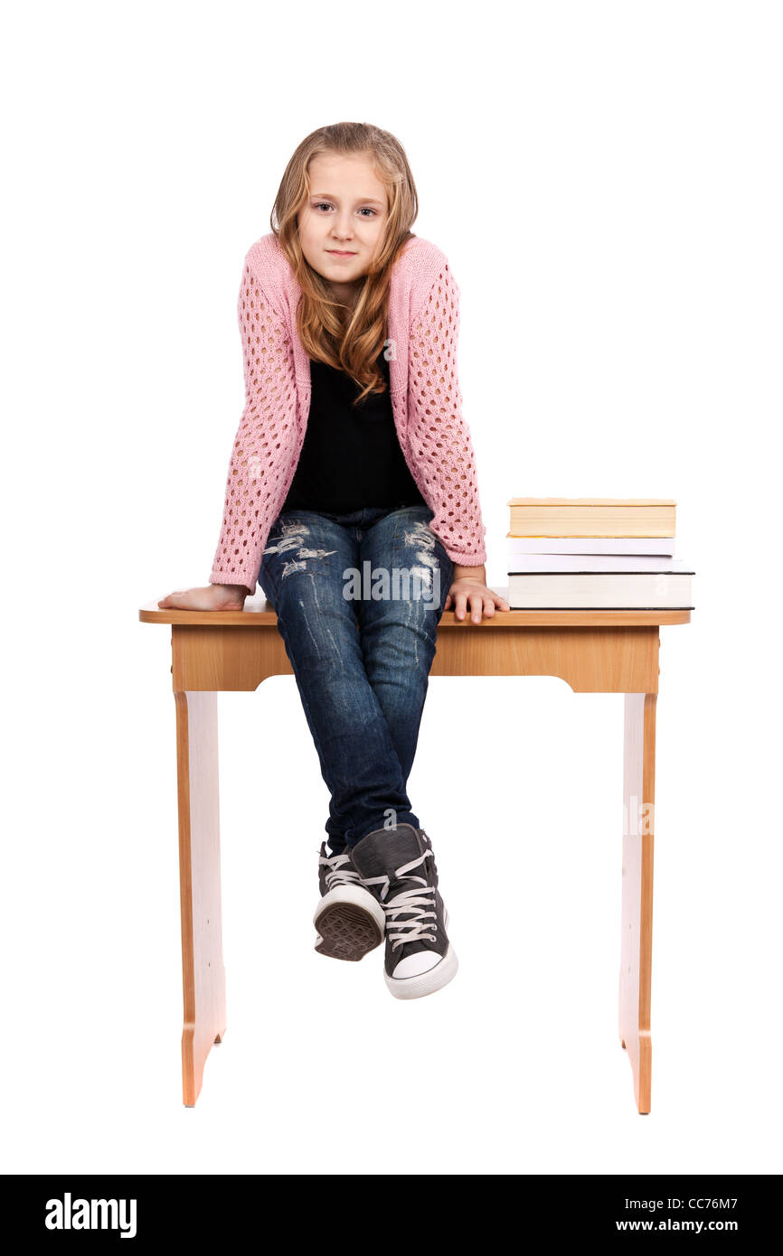 Lindo rubia colegiala sentado en su escritorio con un montón de libros cercano Foto de stock