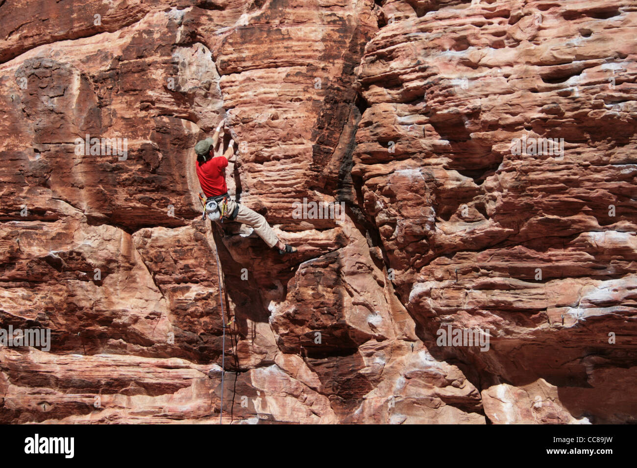 Escalador en rojo escalando un acantilado de arenisca roja en el Red Rocks, Nevada Foto de stock
