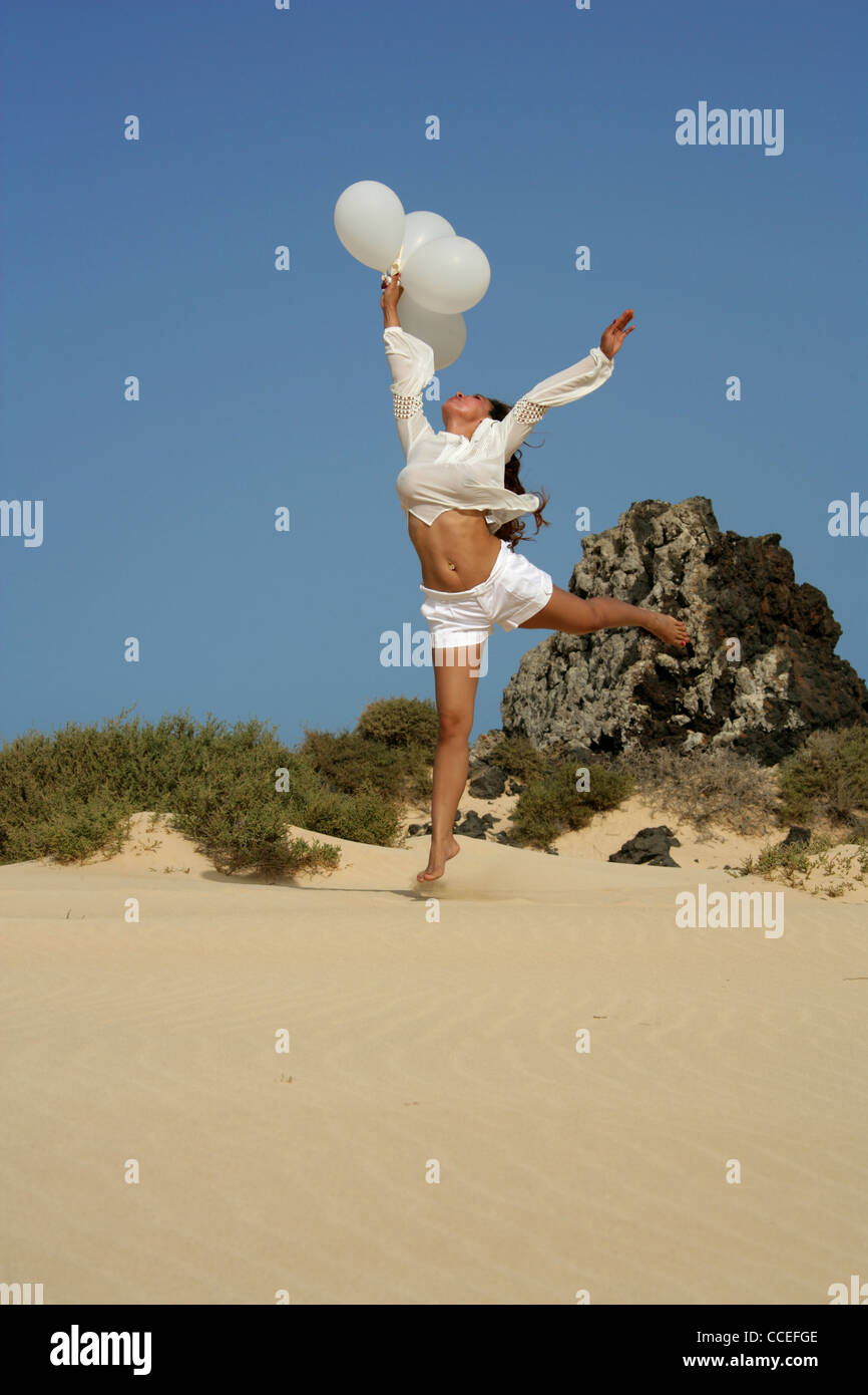 Chica de Indonesia en un traje blanco con globos saltando sobre las dunas de arena, Fuerteventura, Islas Canarias. Foto de stock