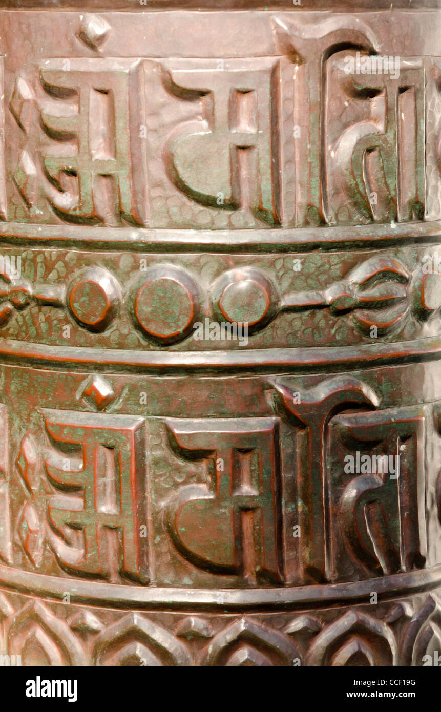 Primer plano de una rueda de oración budista tibetano de bronce con escritura sánscrita con el mantra OM MANI PADME HUM Foto de stock