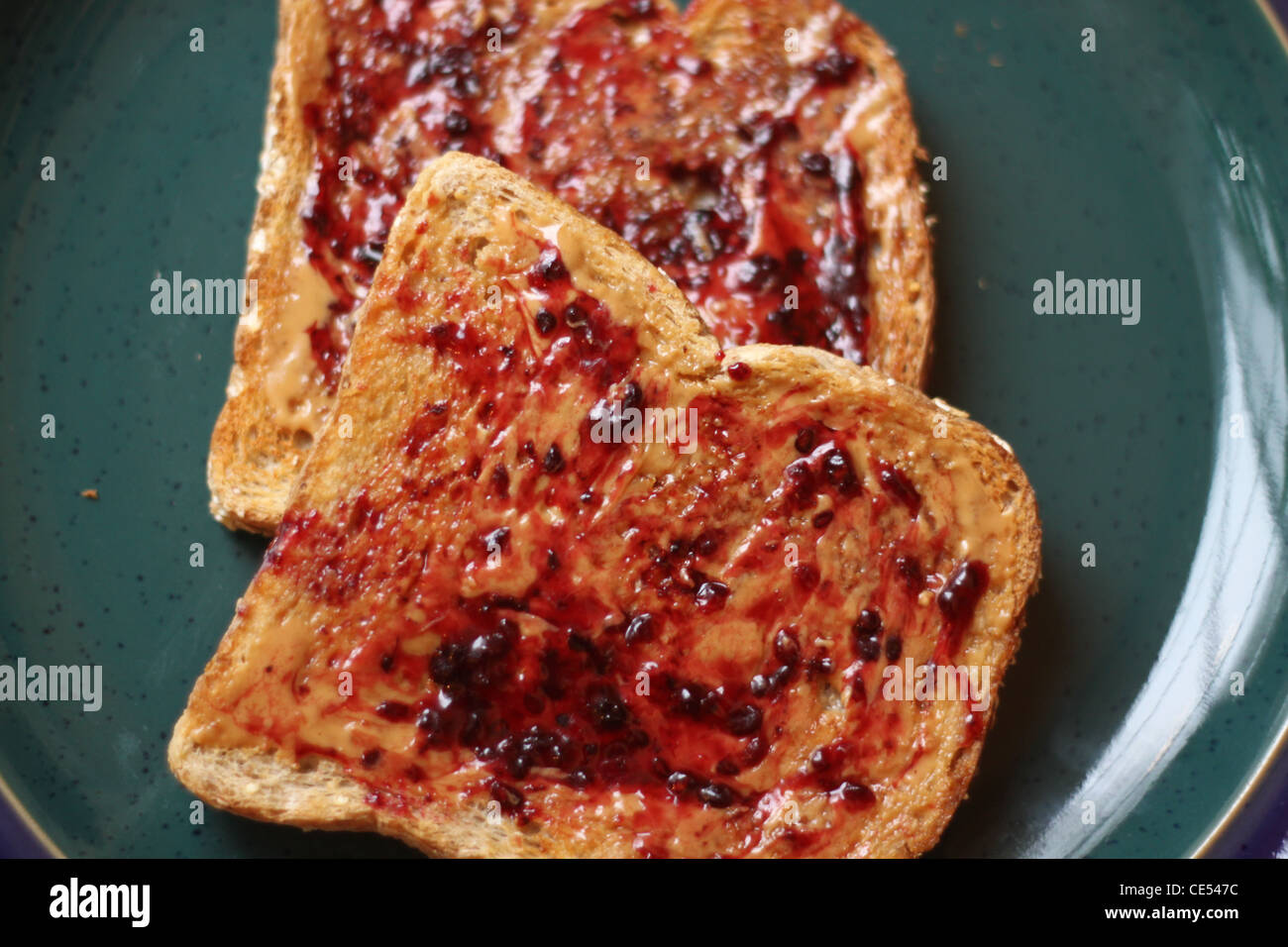 Cara abierta de mantequilla de maní y mermelada trigo tostada sobre una placa verde Foto de stock