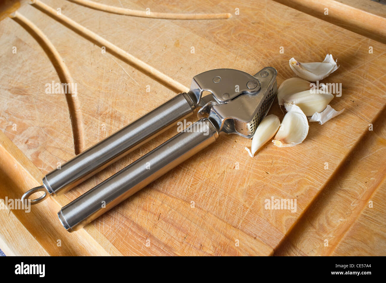Prensa ajos con dientes de ajo sobre una tabla para cortar Foto de stock