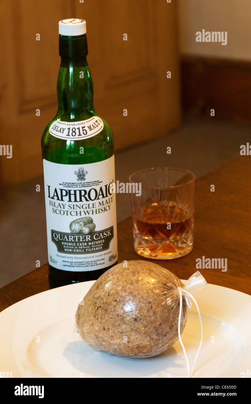Un haggis en una placa, delante de una botella de whisky de malta Laphroaig y un vaso de whisky. Foto de stock