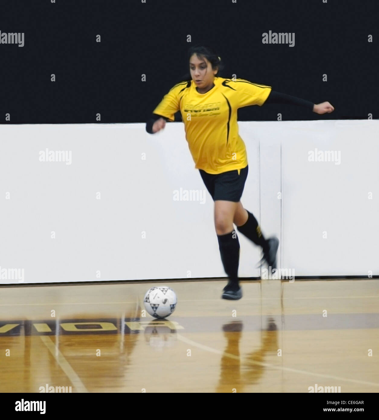 Un joven latino chica hispana jugando fútbol en un gimnasio escolar Foto de stock