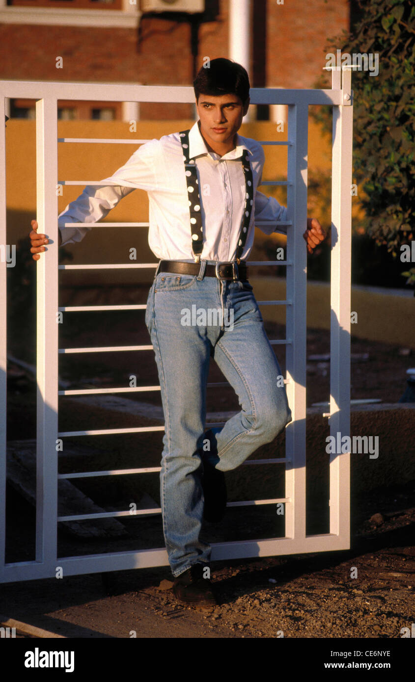 Hombre en blue jeans y camisa blanca recostada contra la puerta de hierro  señor#166 Fotografía de stock - Alamy