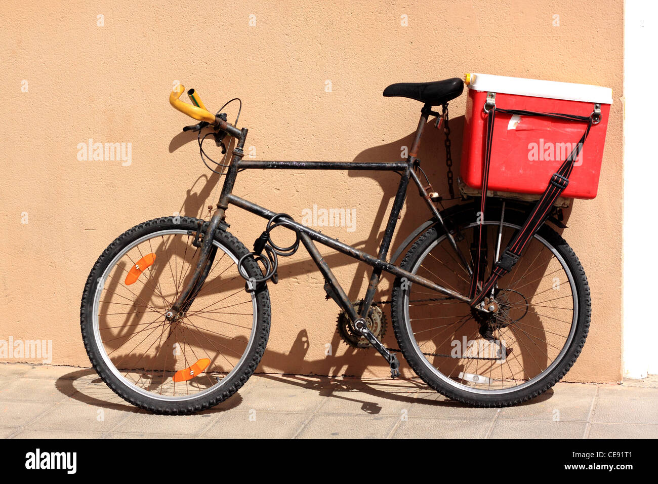 Muy usado bike apoyado contra una pared en color ocre rosa Callajero, Fuerteventura. Foto de stock