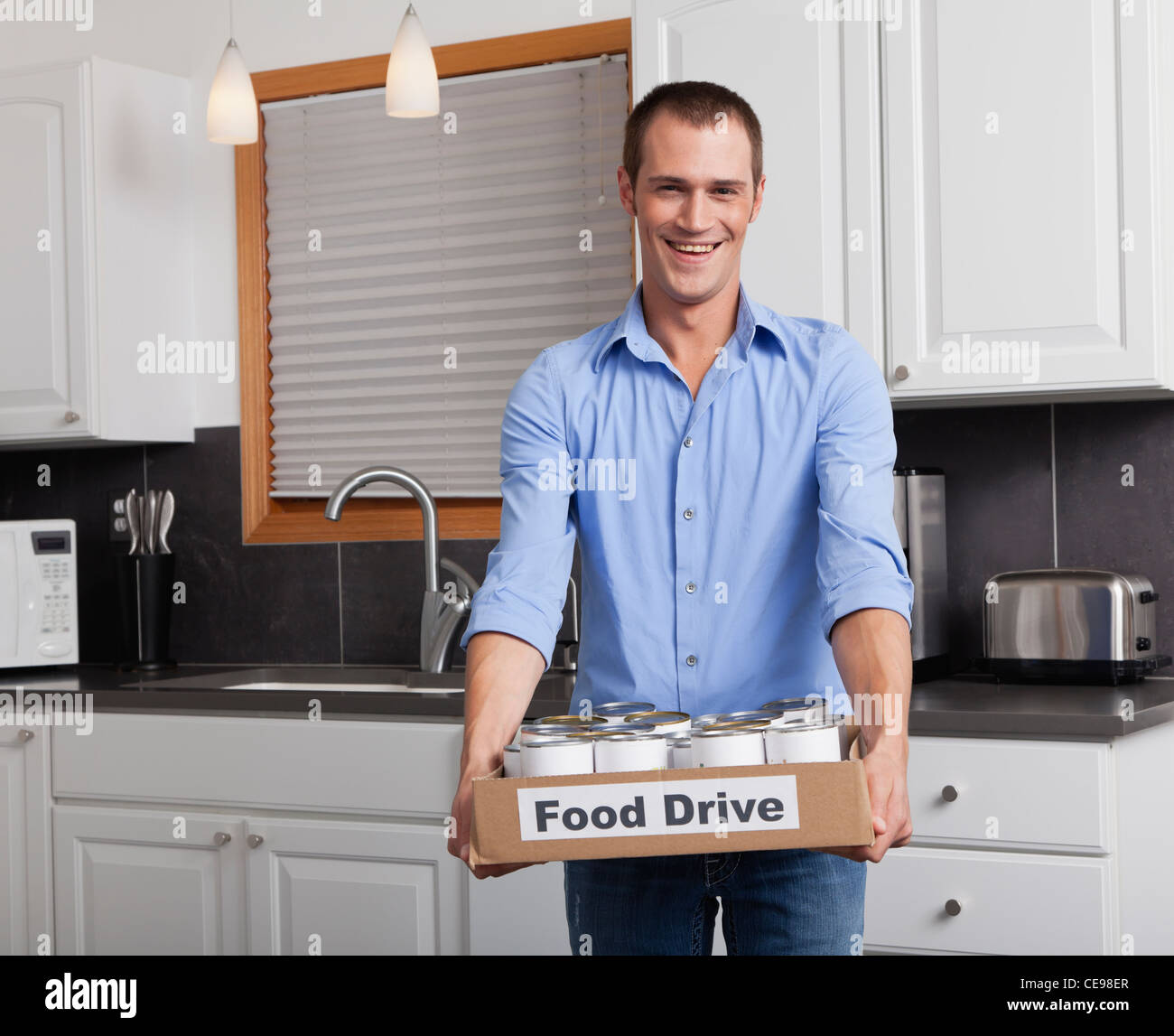 Estados Unidos, Illinois, Metamora, Retrato del hombre sonriente sosteniendo la caja de cartón con los alimentos enlatados en la cocina Foto de stock