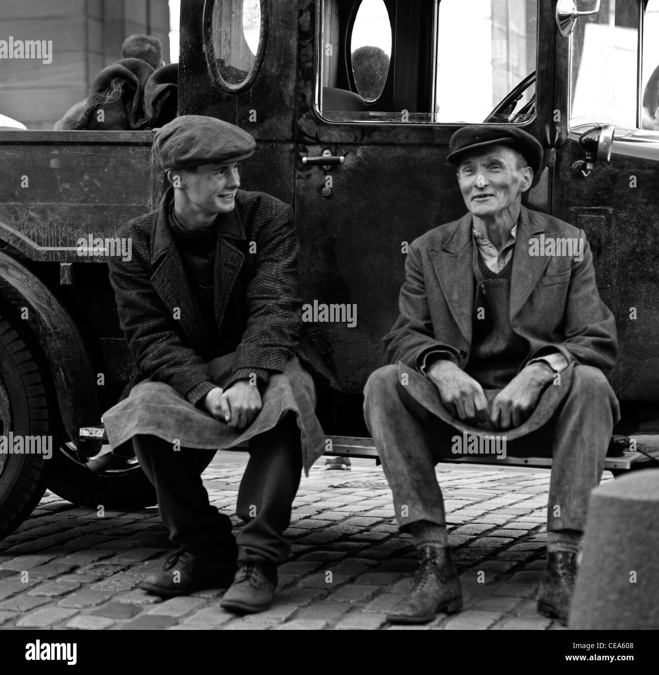 Hombre y niño en vintage trajes vestidos como coalmen sentado en el paso del viejo camión Edimburgo Scotland Reino Unido monocromo Foto de stock