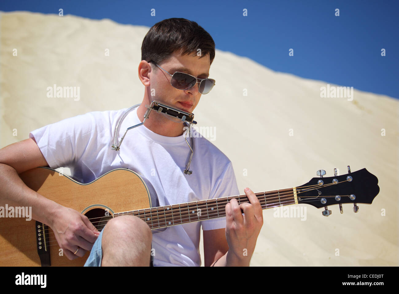 Chico en gafas de sol toca la guitarra y acordeón labio sentados sobre  arena Fotografía de stock - Alamy