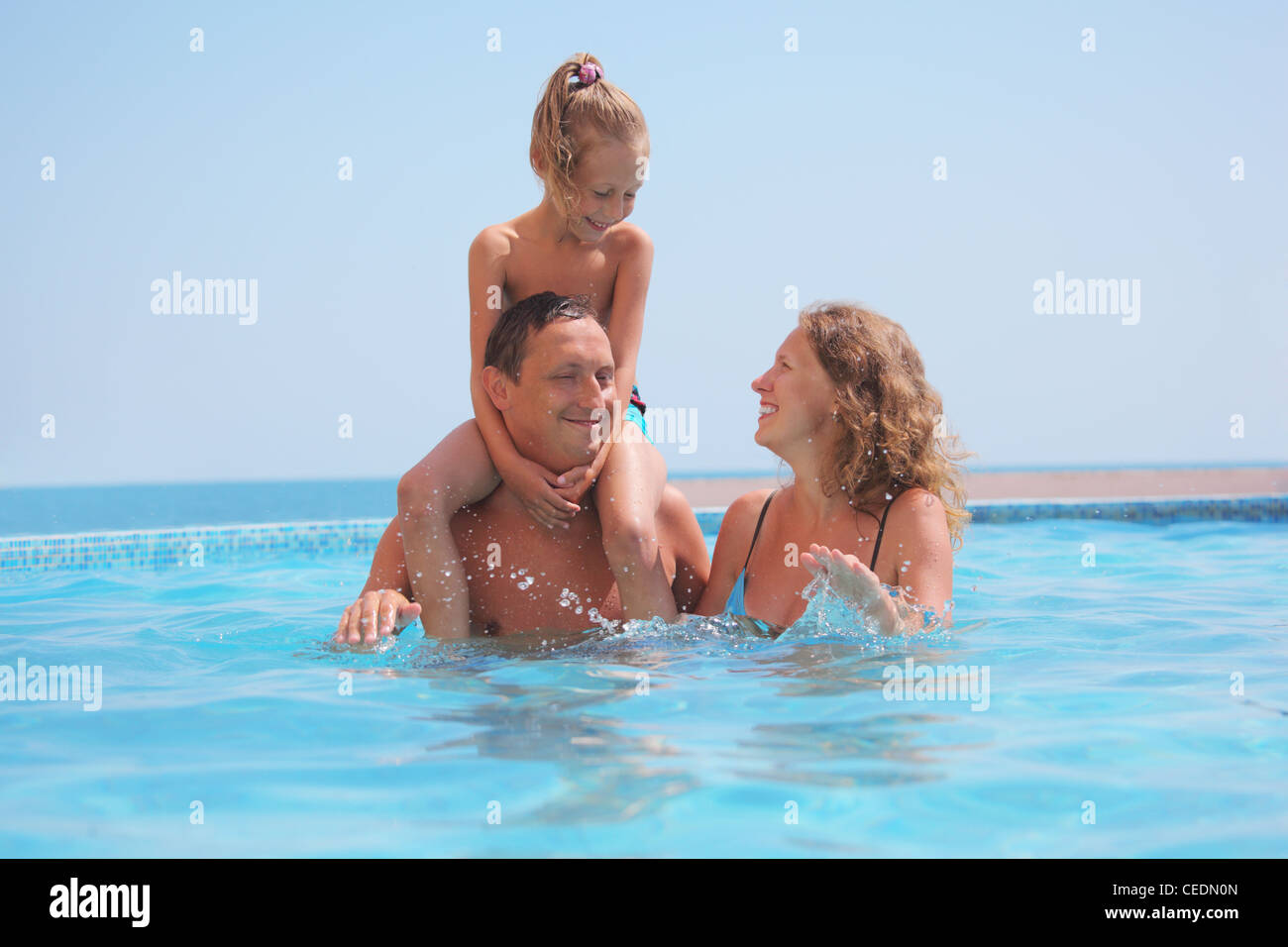 Familia feliz en la piscina en el fondo del mar. Hija descansa sobre los hombros de los padres Foto de stock