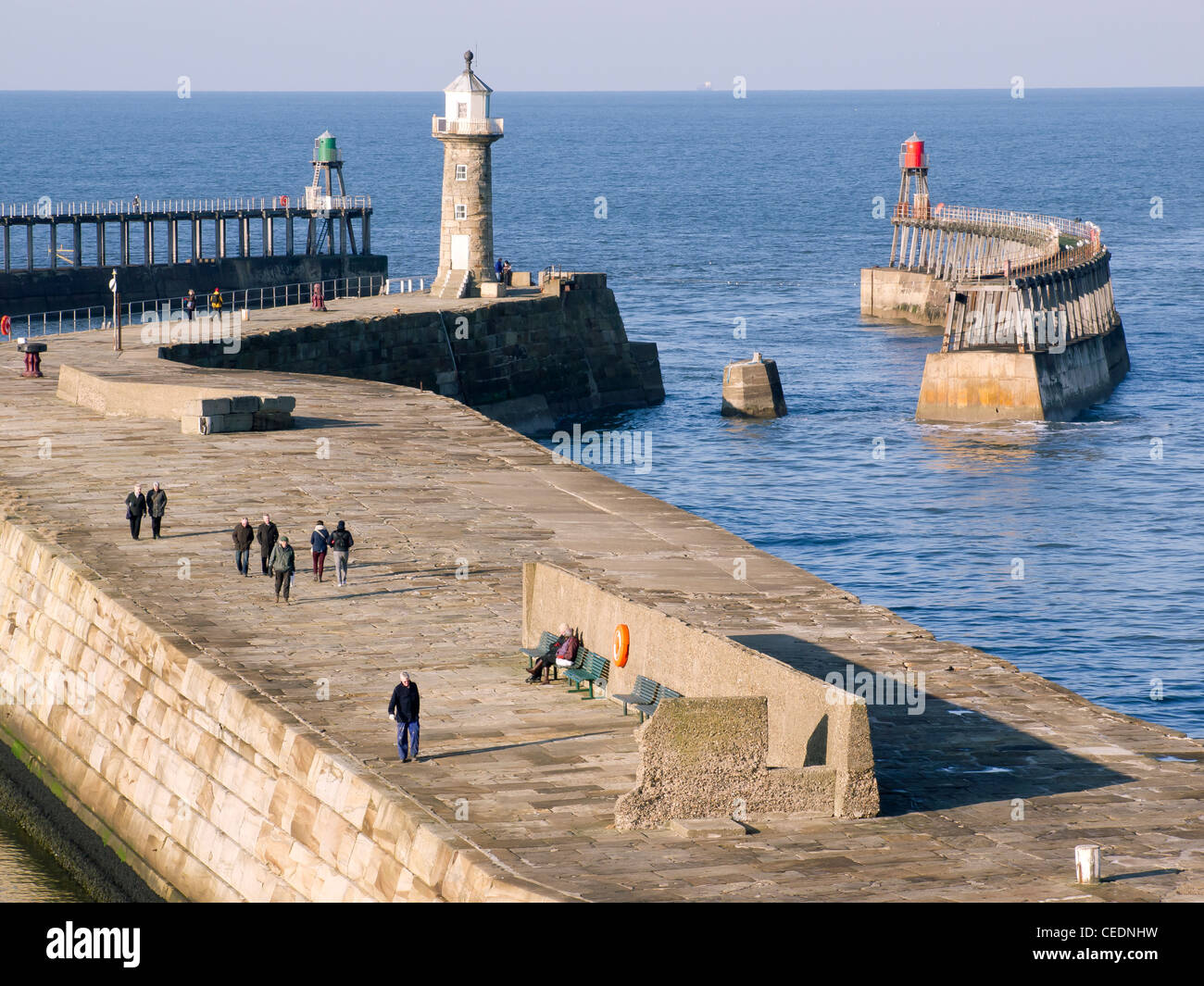 La gente disfruta de un paseo en Whitby East Pier en un soleado día de invierno Foto de stock