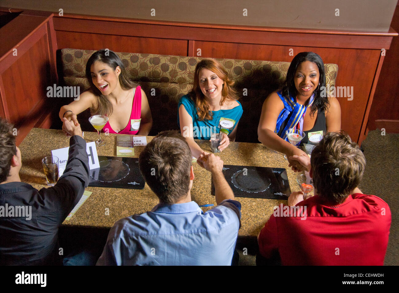 Las parejas se estrechan las manos mientras el speed dating en un restaurante de California Foto de stock
