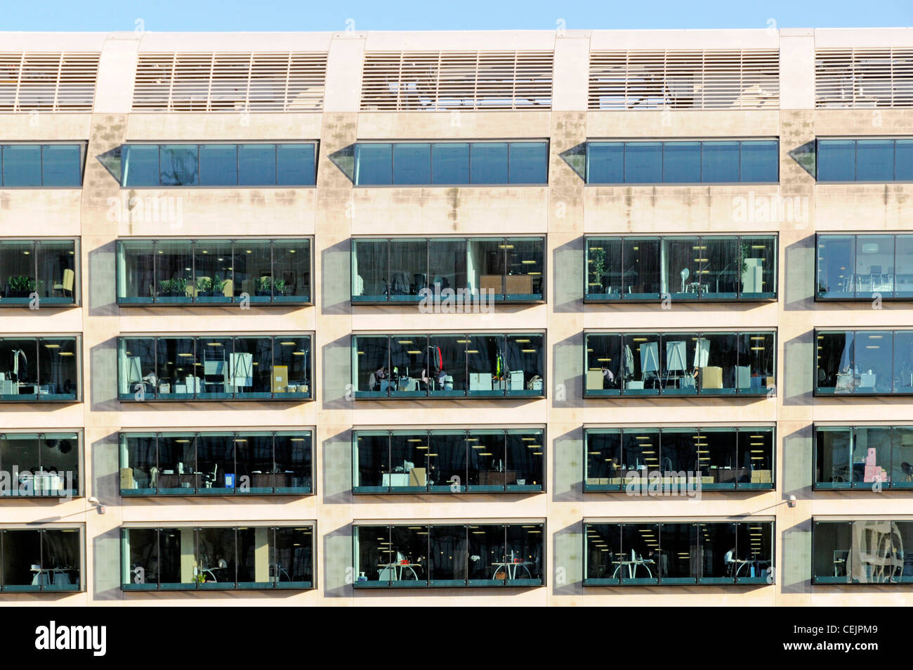 Bloque de oficina a través de windows vista desde el exterior a la luz del día con luces interiores en la ciudad de Londres, Inglaterra Foto de stock
