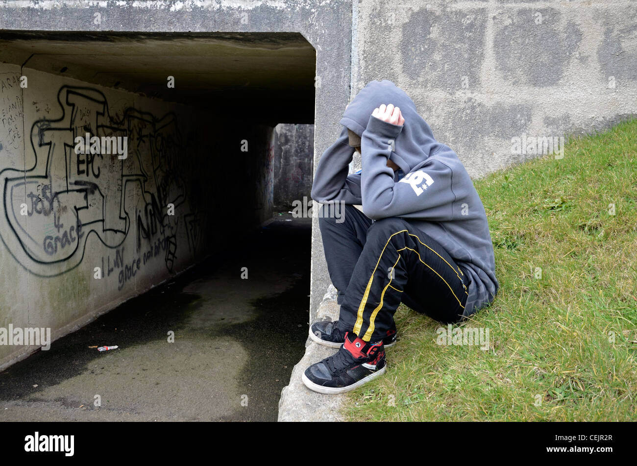 Un muchacho tenage sosteniendo su cabeza en sus manos se sentaba fuera un paso subterráneo Foto de stock