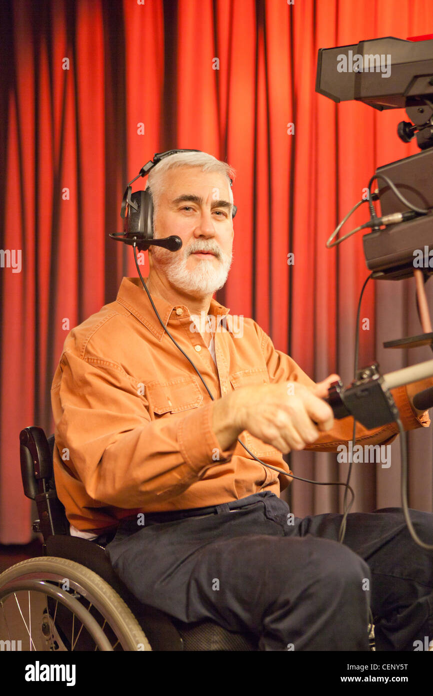 Hombre en silla de ruedas con distrofia muscular mediante una cámara de televisión y un teleprompter en studio Foto de stock