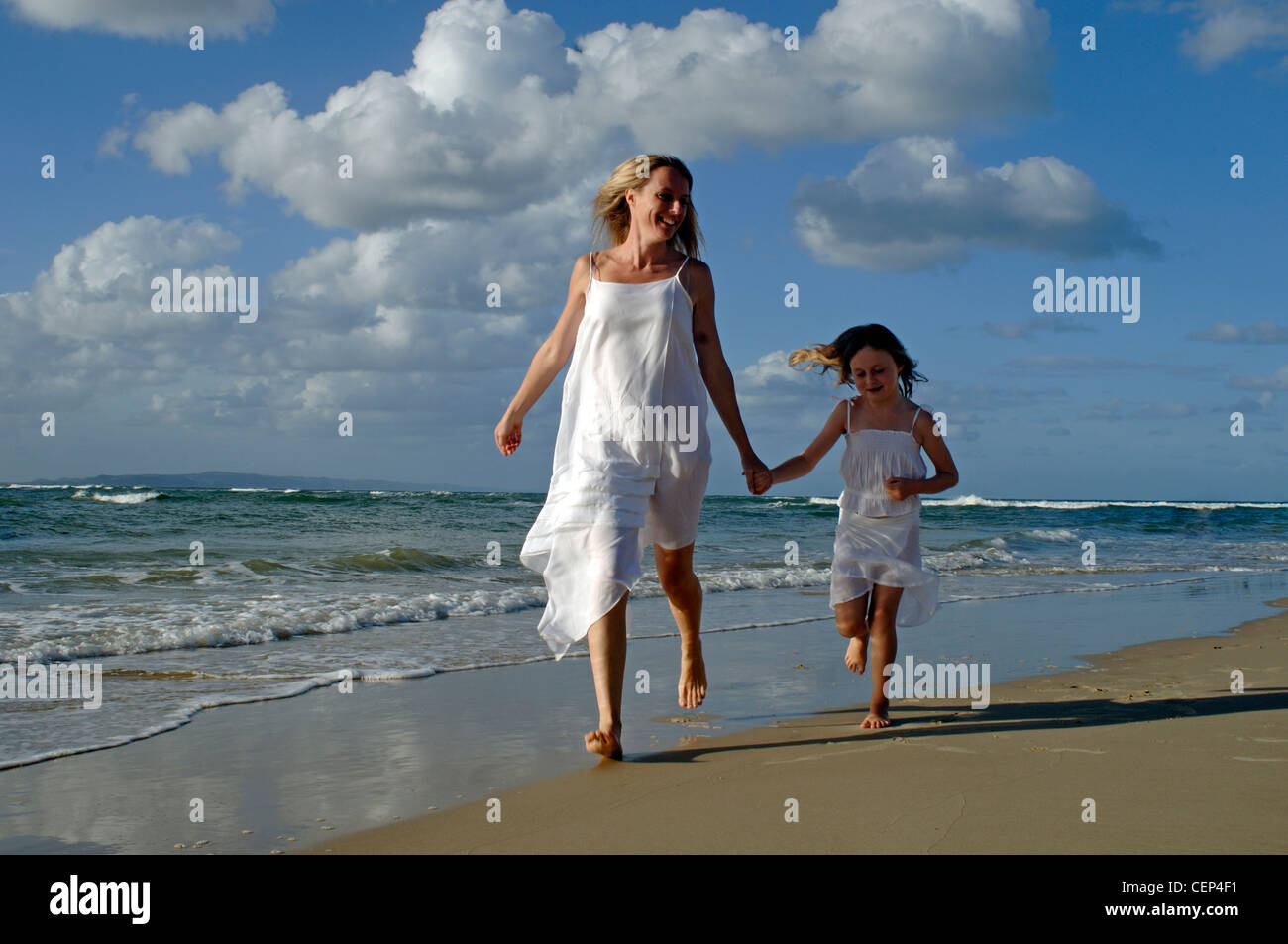 Madre e hija luciendo vestidos blancos en una playa que corre a lo largo de manos Fotografía de - Alamy