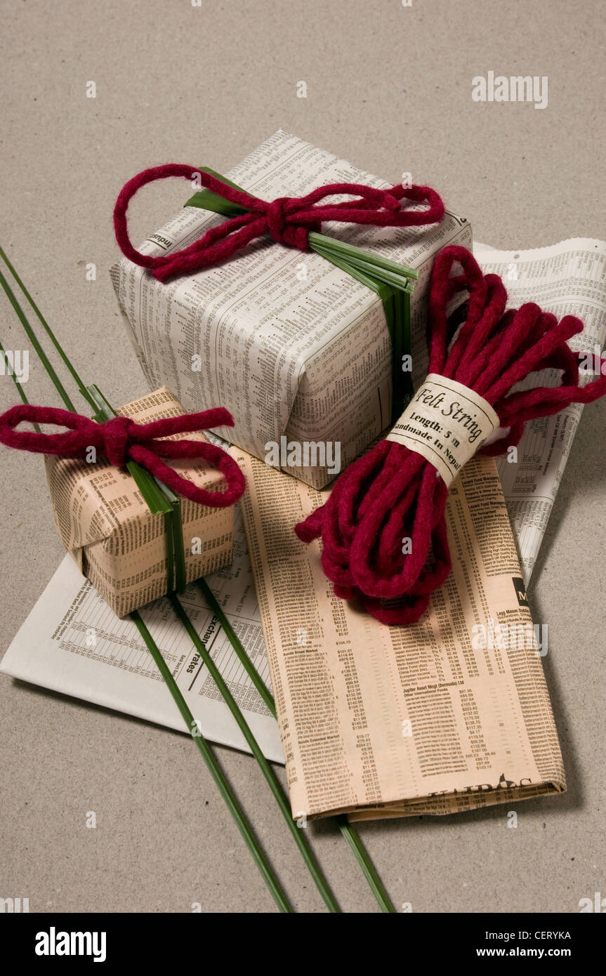 Un bodegón de regalos envueltos en papel de periódico de hierba de acero  envuelto alrededor del centro y se mantienen en su lugar por un fieltro de  Borgoña Fotografía de stock -