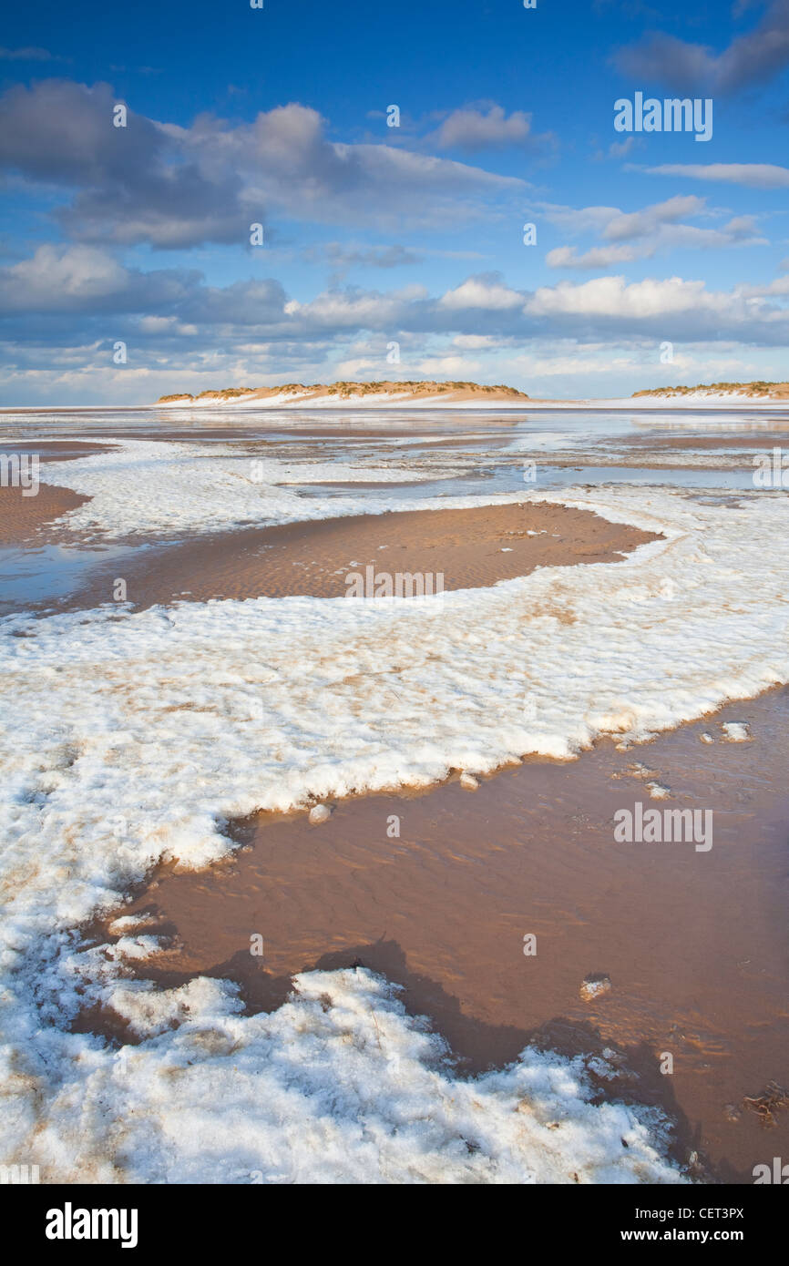 La nieve que queda en la playa de la marea entrante en pozos junto al mar en el norte de la costa de Norfolk. Foto de stock