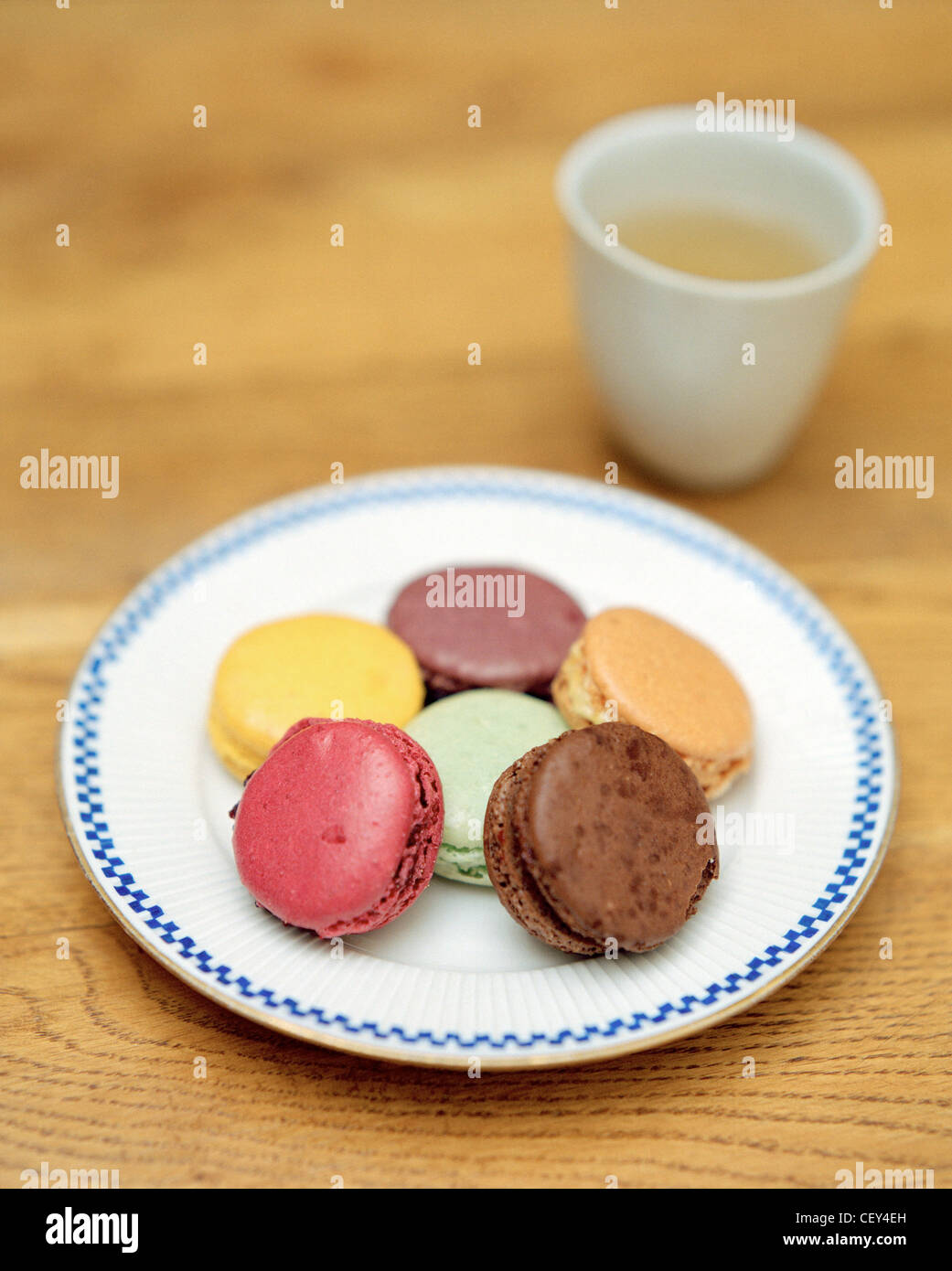 Macarons multicolor en la placa con una pequeña taza de té en el fondo Foto de stock