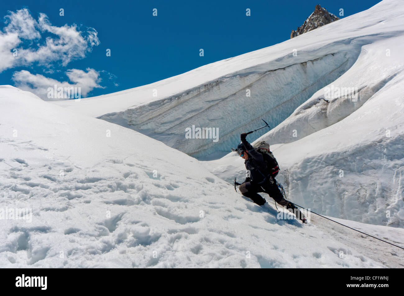 Un escalador masculino , vestida de negro, sube una pendiente de nieve. Día de cielo claro de invierno. Foto de stock