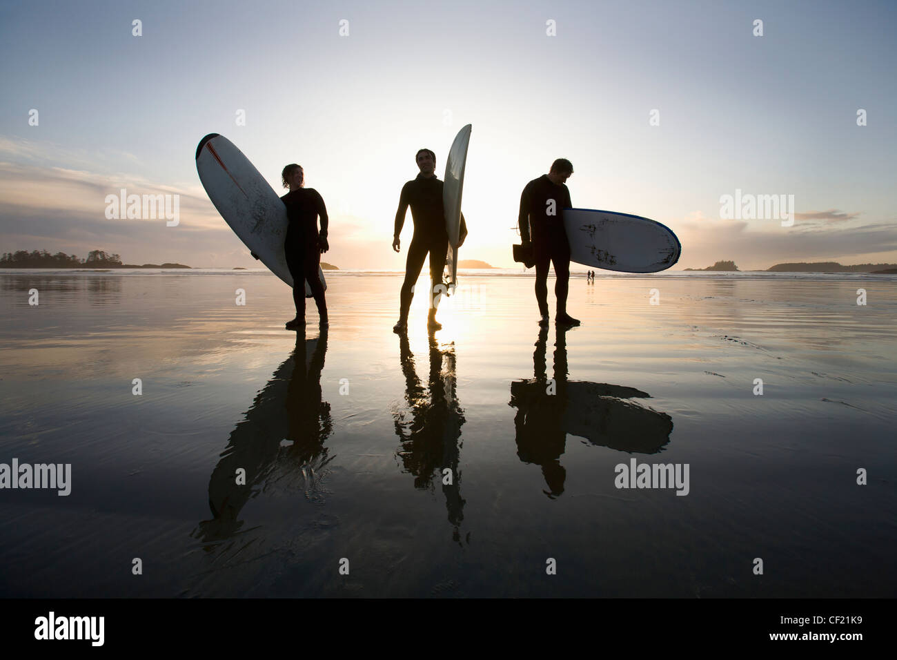 Silueta de tres surfistas llevar tablas de surf; Chesterman Beach Tofino en la isla de Vancouver British Columbia Canadá Foto de stock