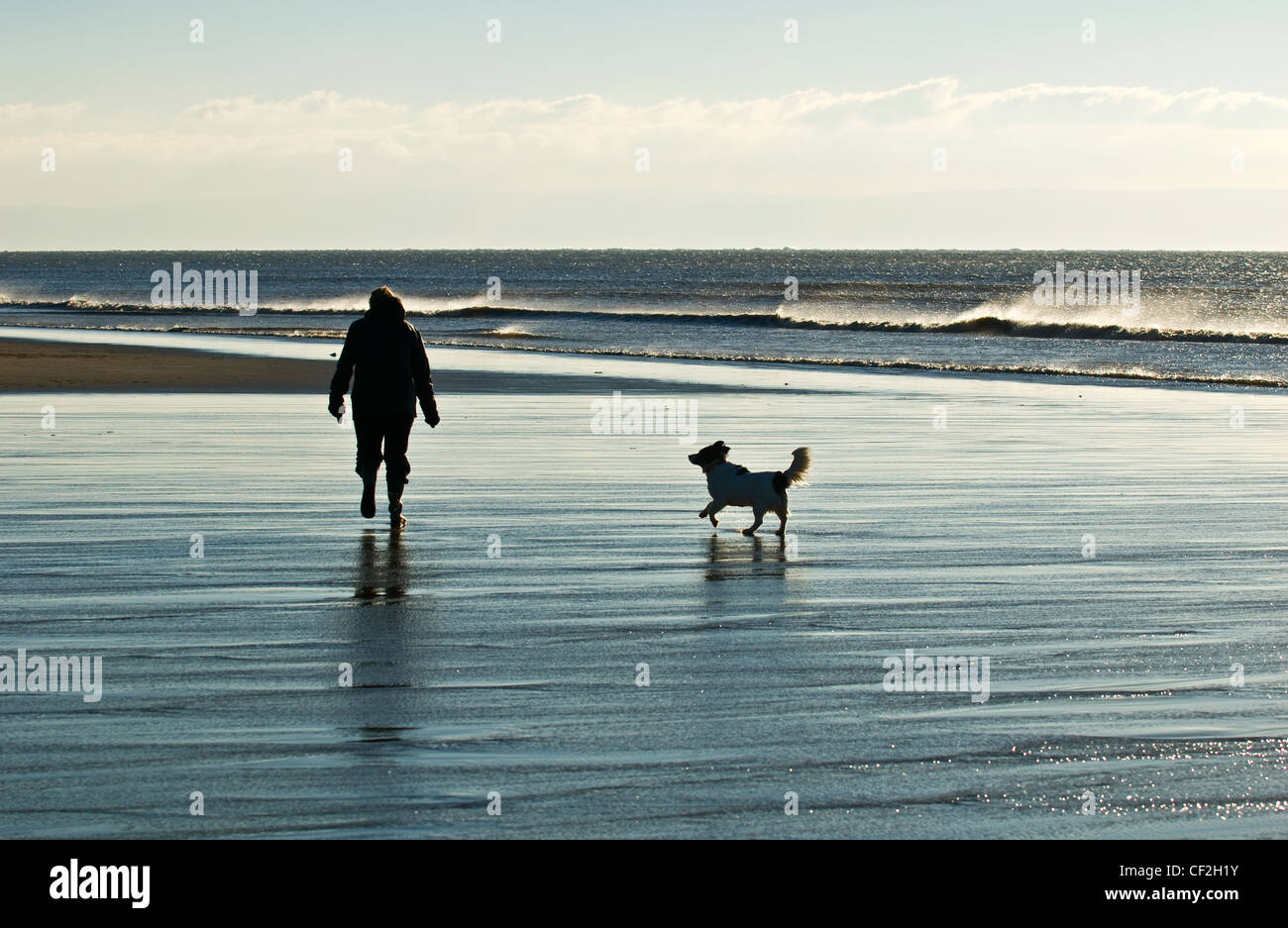 Una persona caminando a su perro a través de la playa en la Bahía de Dunraven. Foto de stock