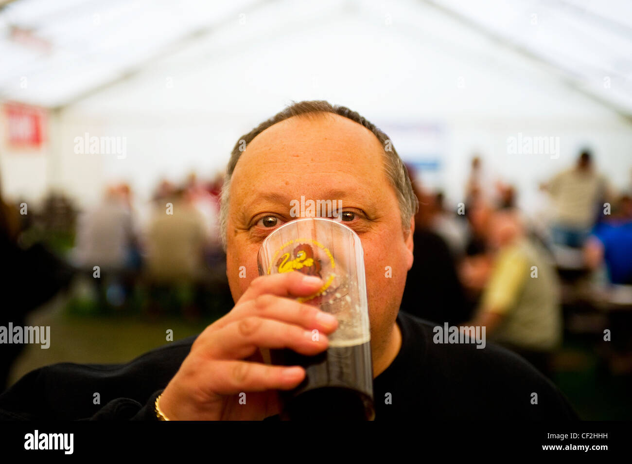 Un hombre bebiendo una pinta de cerveza real dentro de una carpa en el Festival de la cerveza de aro. Foto de stock